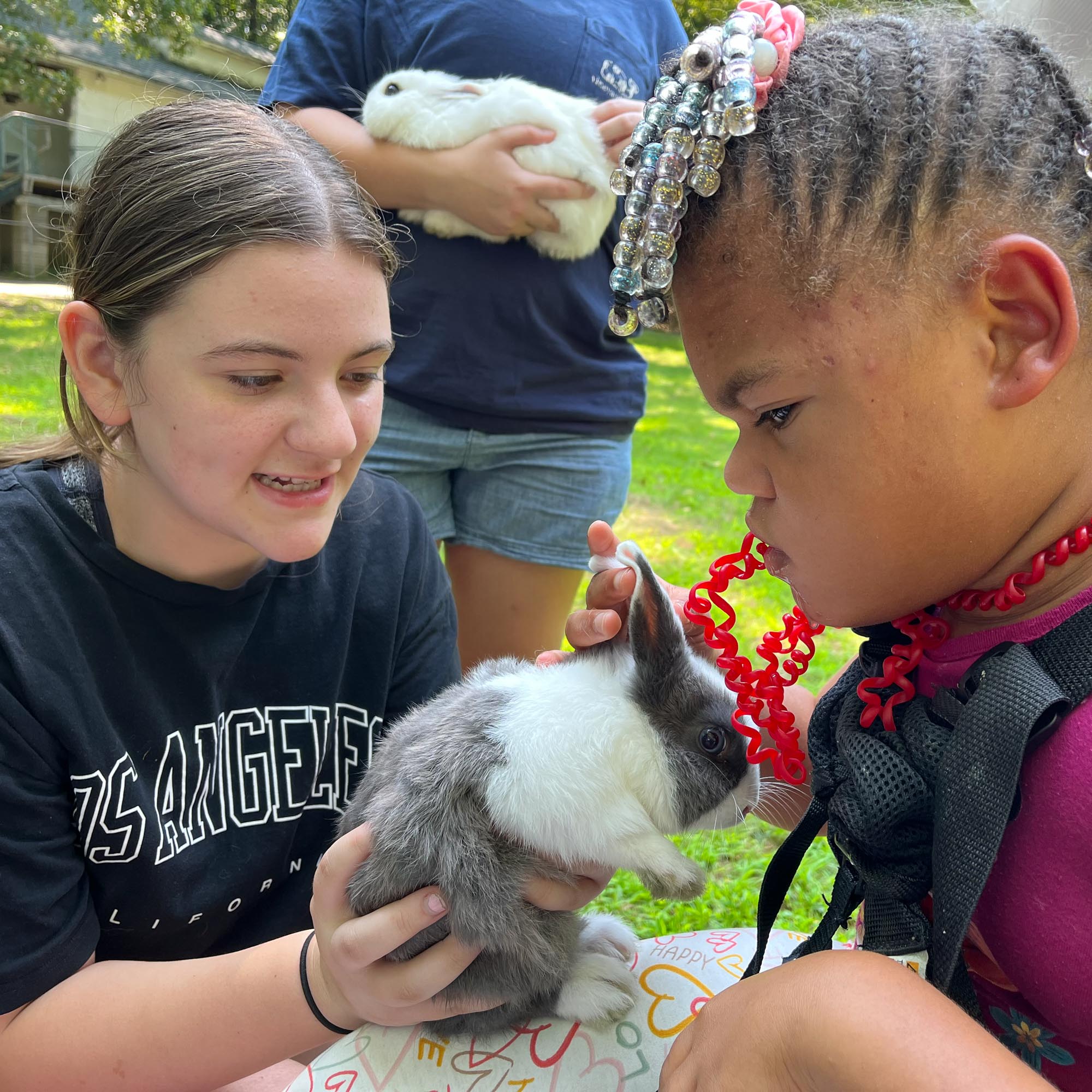 Photo of two young girls holding a black and white rabbit at a petting zoo.