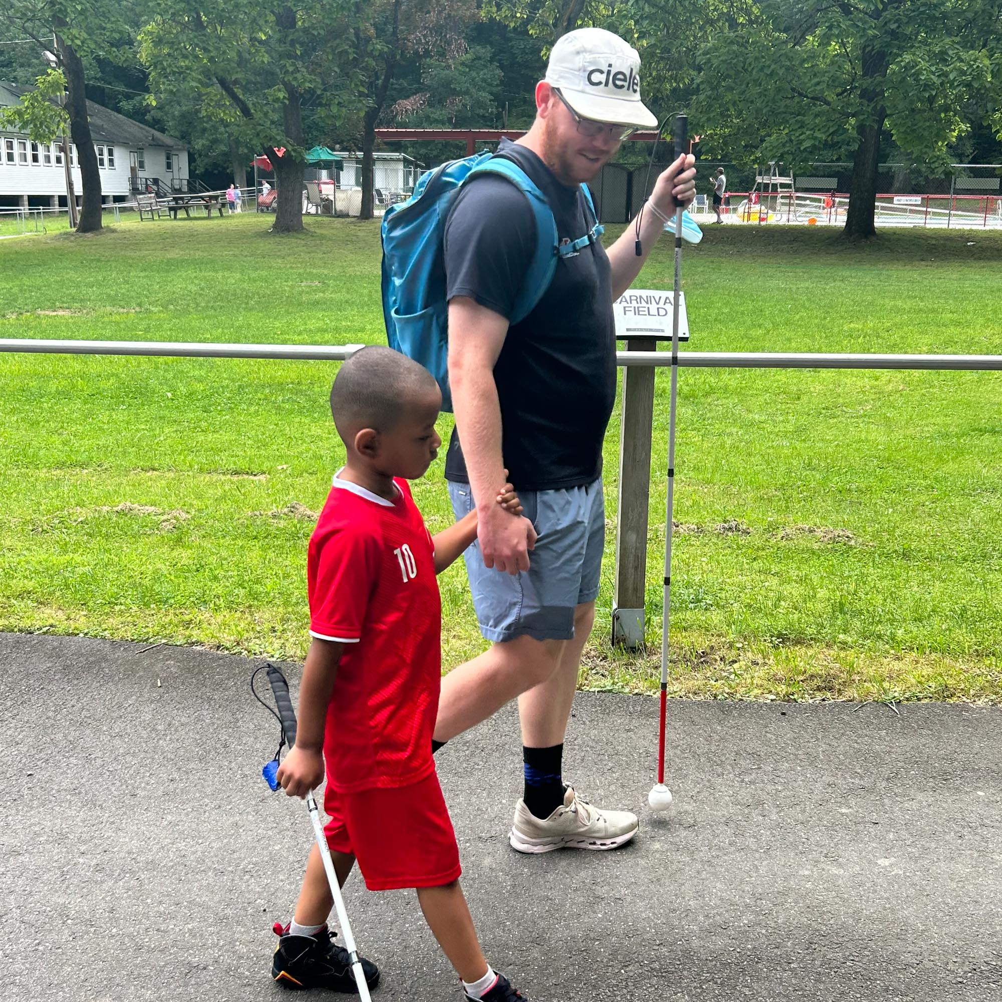 Photo of an Orientation & Mobility instructor holding the hand of a young boy as he walks with his cane.