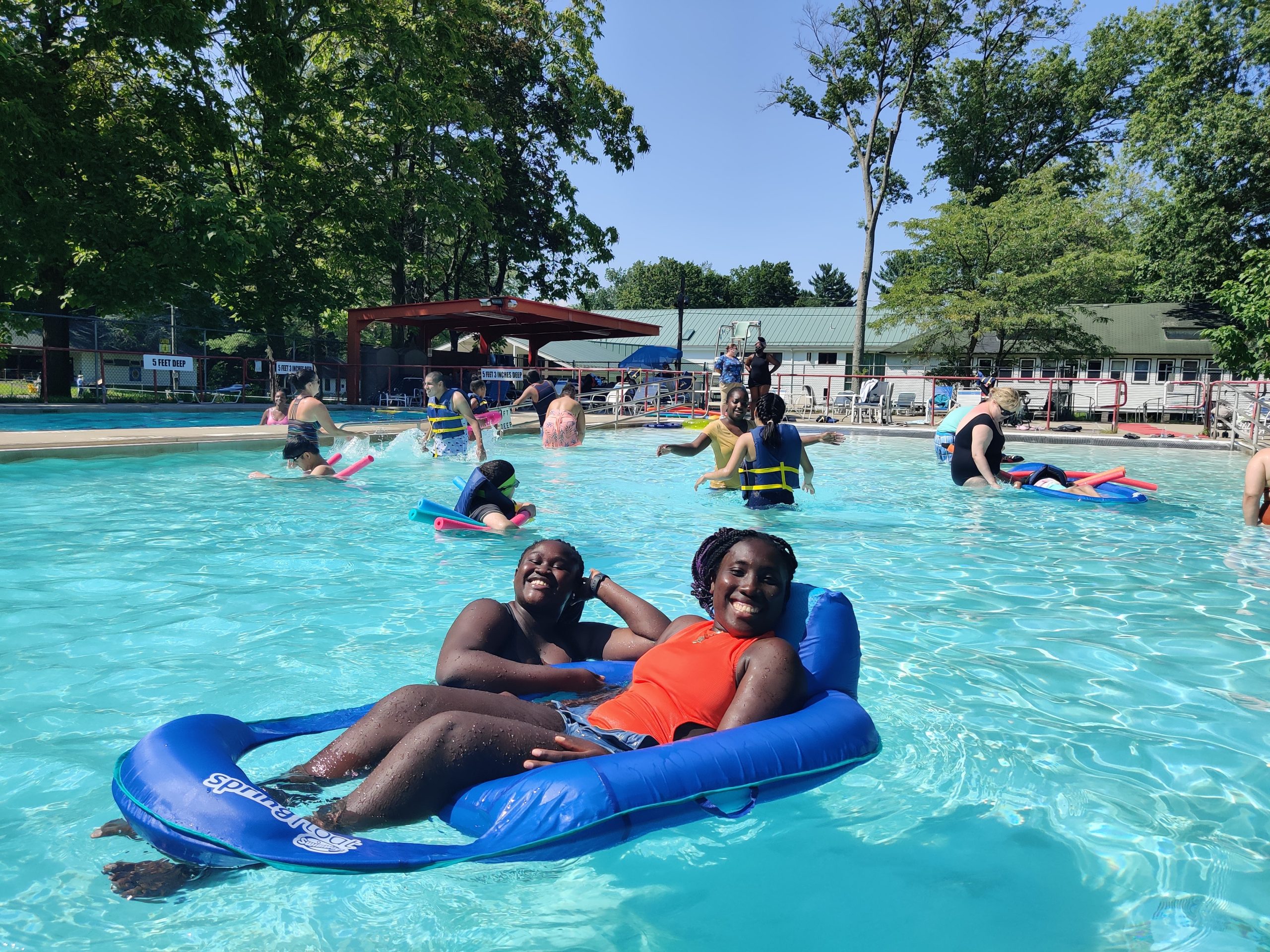 Two participants on a giant raft float in a pool toward the camera and smile.