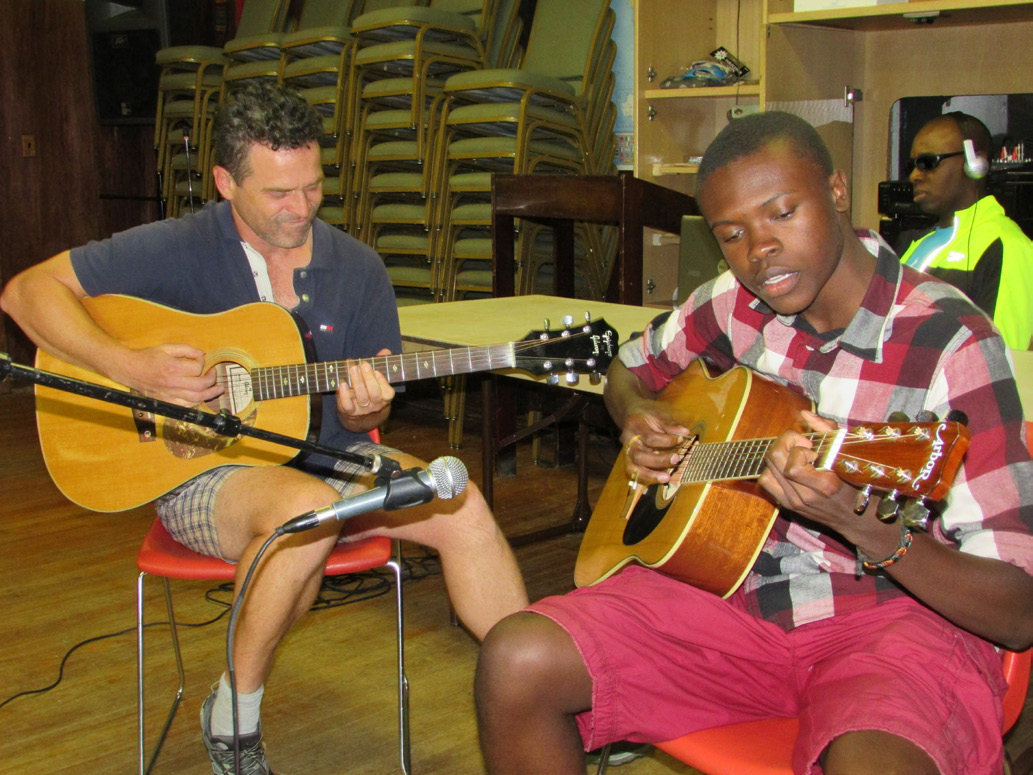 two guys strumming acoustic guitars in empty gymnasium