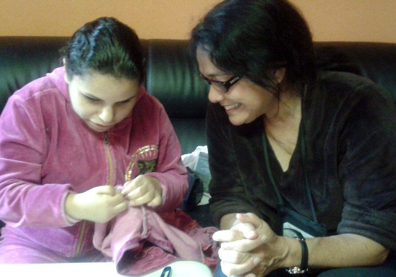 Lady in black helping girl in pink to sew