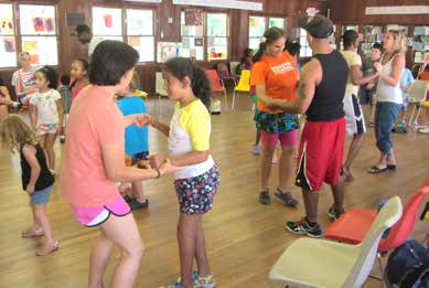 Paired dancers of all ages moving to the rhythm in a well lit hardwood pavilion