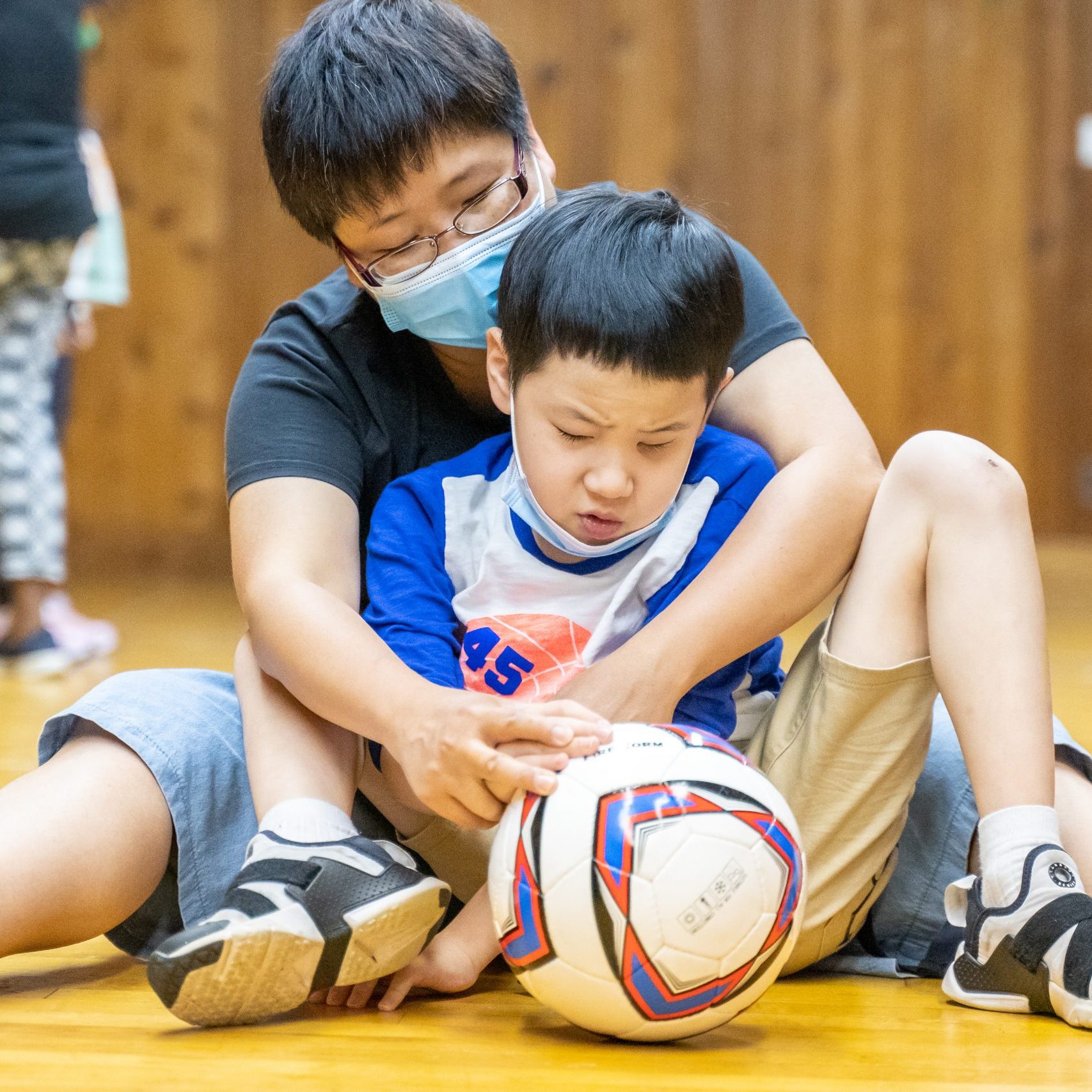 Photo of a VISIONS instructor helping a participant roll a ball at the gym at VISIONS Center on Blindness.