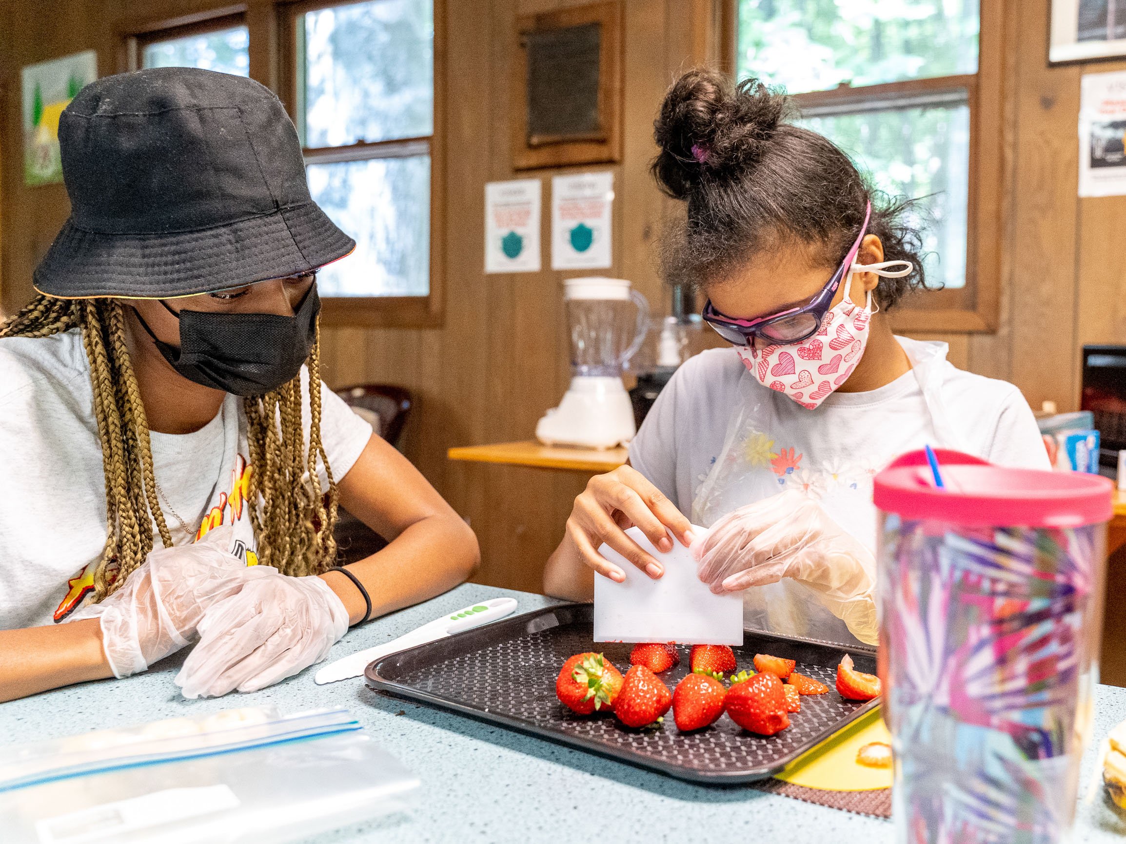 A young girl sits with an instructor and learns how to safely cut strawberries with an adapted cutting tool.