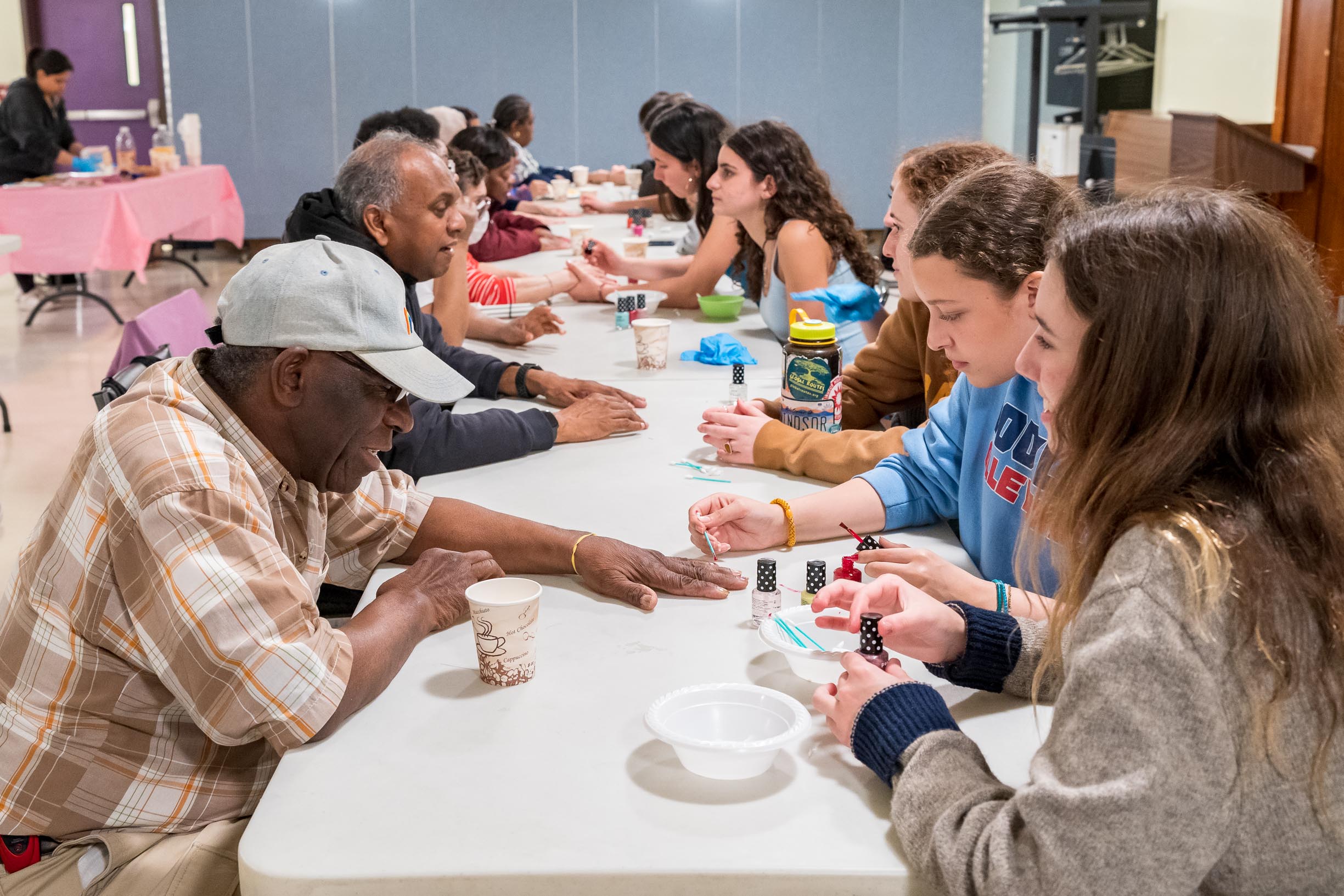 Photo of a group of high school students from GlamourGals, giving manicures to older adult participants sitting across from them.