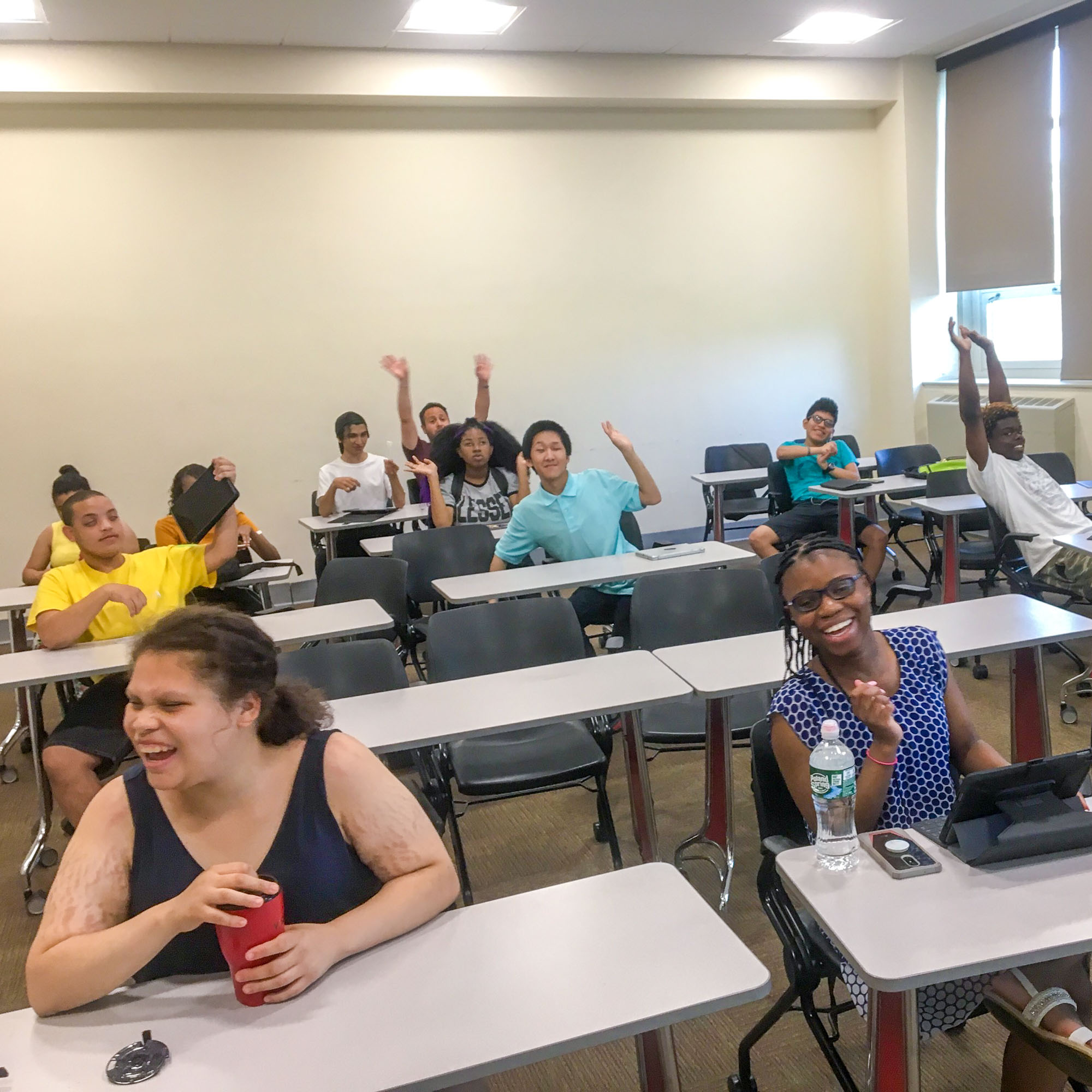 In a classroom, a group of cheerful smiling participants sit at group desks.
