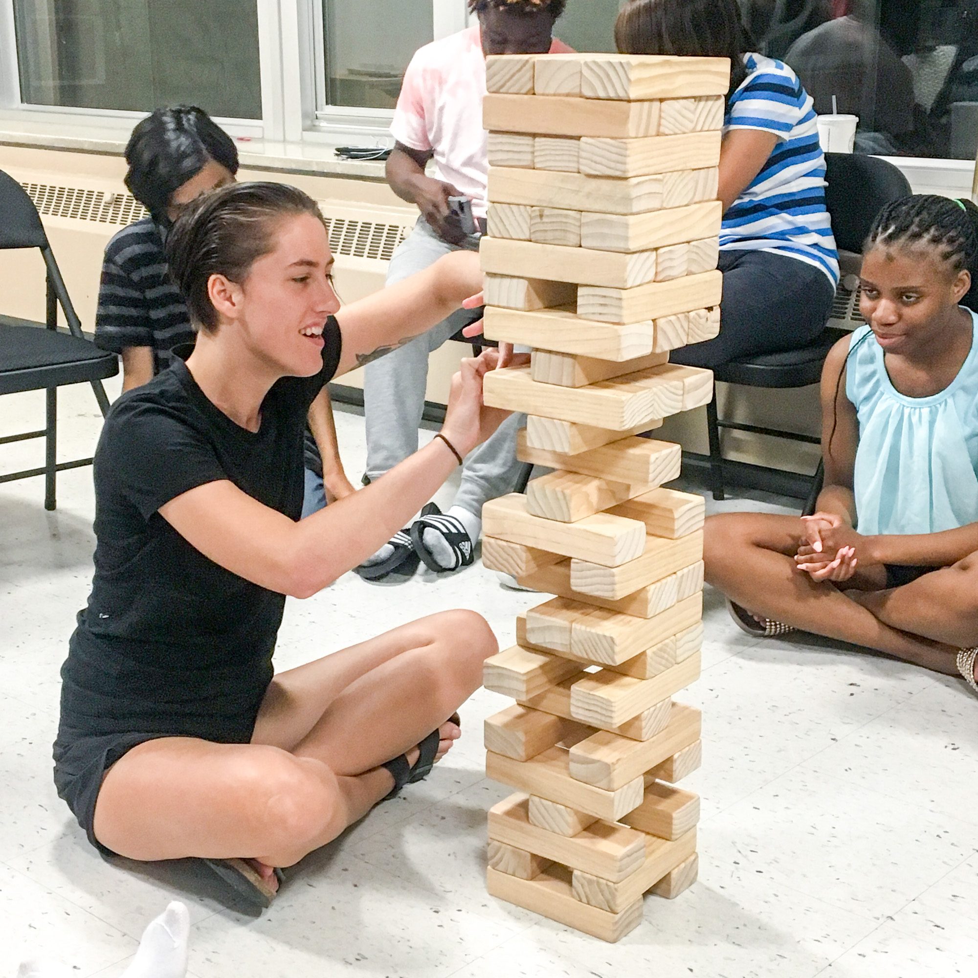 A staff member (left) and participant (right) sit with their legs crossed and play a game of giant Jenga.