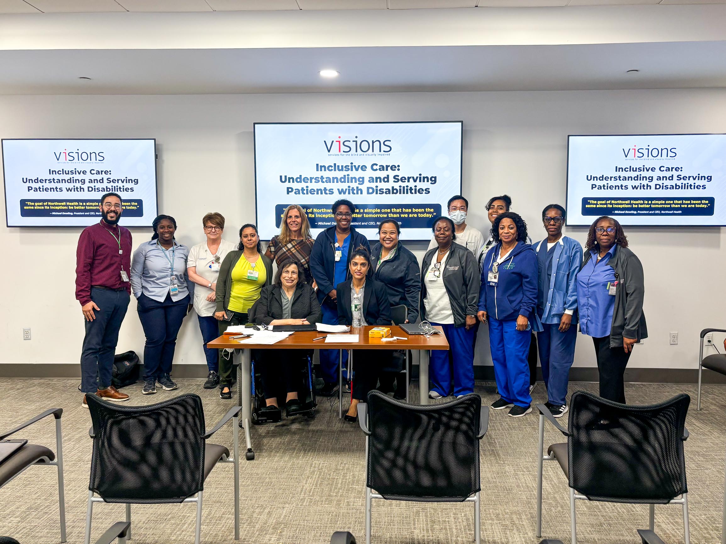 Group photo of VISIONS and Northwell Health staff standing together, underneath a presentation screen that reads "Inclusive Care: Understanding and Serving Patients With Disabilities".