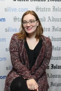 Image of Victoria Priola, standing in front of a step-and-repeat and smiling to the camera.