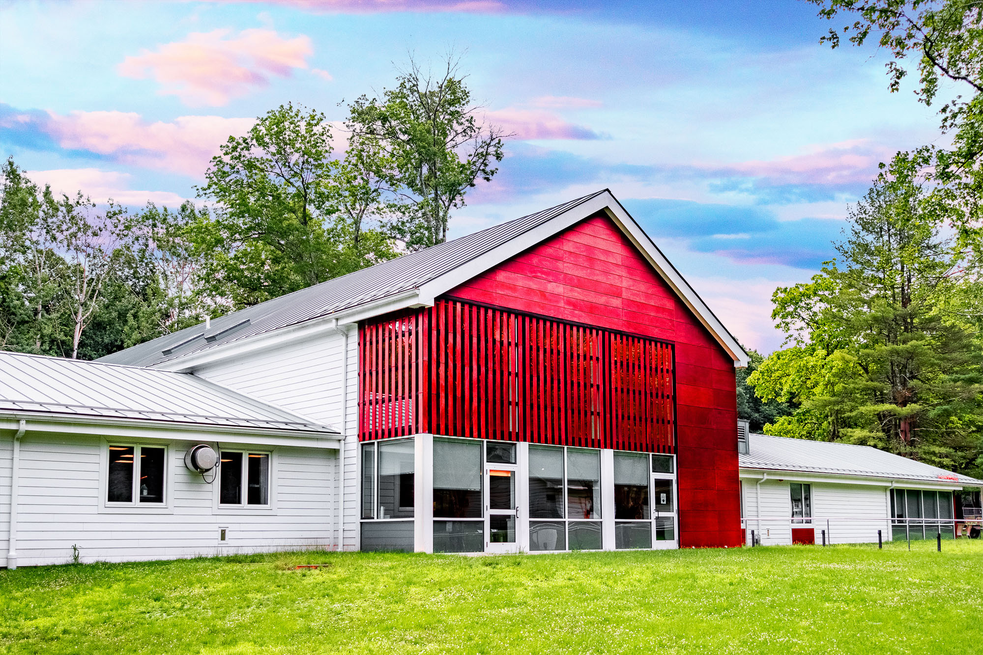 Exterior shot of VISIONS Vocational Rehabilitation Center, a large red and white barn-shaped house, surrounded by grass and trees.